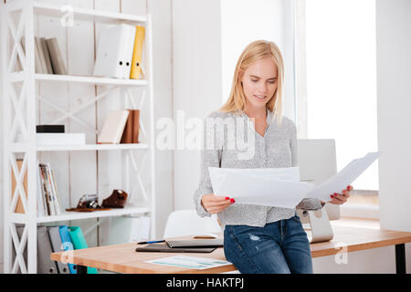 Junge hübsche Geschäftsfrau auf den Schreibtisch zu sitzen und Lesen von Dokumenten Stockfoto