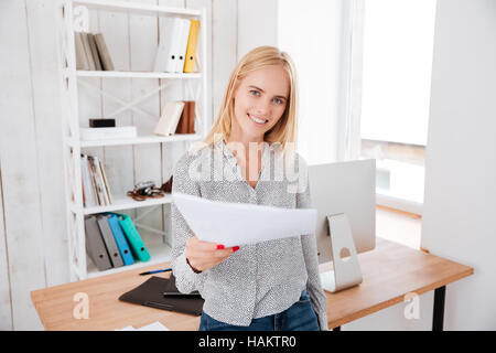 Glücklich lächelnd Business-Frau sitzt am Schreibtisch und Kamera Dokument verleiht Stockfoto