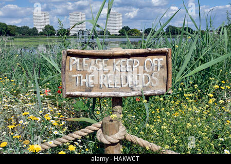 Ein Schild am Woodberry Feuchtgebiete, Hochhäusern des Weingutes Woodberry Down in der Ferne umgeben von wilden Blumen und Röhrichten. Stockfoto