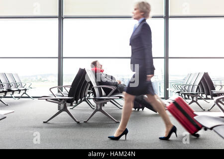 Geschäftsfrau ziehen Koffer Vergangenheit ruhen Geschäftsmann mit Nackenkissen im Abflugbereich des Flughafen Stockfoto