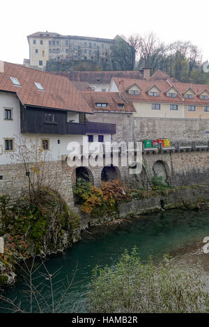 Häuser in Blazeva Ulica (Straße) am Ufer des Flusses Selca Sora mit Skofja Loka Schloss Skyline. Skofja Loka, Slowenien Stockfoto