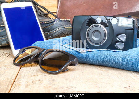 Reisen Sie casual-Outfits mit Kamera, Smartphone, Schuhe, Geldbörse, Ledertasche, Sonnenbrille und Jean auf Holztisch. Reisekonzept. Stockfoto