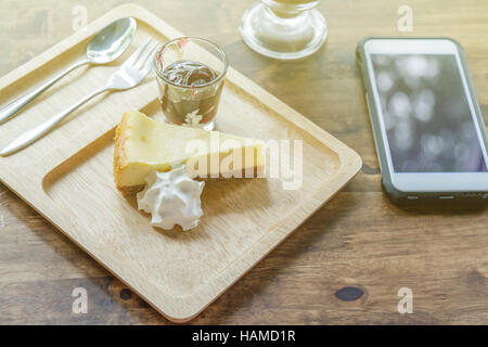 Blaubeer-Käsekuchen mit Sahne auf Holzplatte und einen Kaffee- / Smartphone im Restaurant. Sonnenlicht. Stockfoto