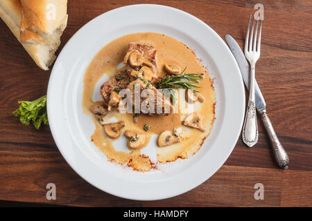 Konzept: Speisekarten, gesundes Essen, hausgemachte, Feinschmecker, Völlerei. Weißen Teller mit Schweinsmedaillons mit Pilzsauce auf verwitterten Holztisch Stockfoto
