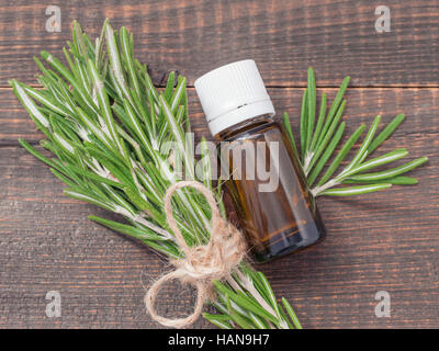 Rosmarin ätherisches Öl in dunkle Glasflasche und frischem Rosmarin auf dunklem Holz. Draufsicht oder flach legen Stockfoto