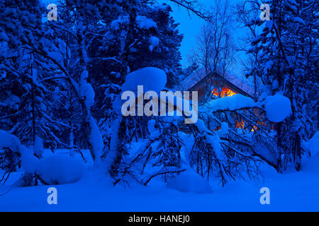 Winterabend in den Wäldern. Viel Schnee. Beleuchtete Hütte im Hintergrund Stockfoto