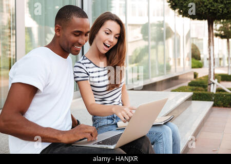 Multiethnische junge Brautpaar zu sprechen und mit Laptop im freien Stockfoto