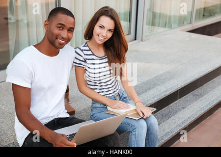 Fröhliche multiethnischen junges Paar sitzt und mit Laptop im freien Stockfoto