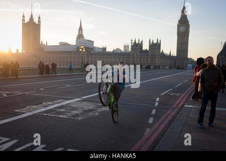 Ein Jüngling balanciert auf sein Hinterrad durchführen einen Wheelie auf der südlichen Seite der Westminster Bridge, am 30. November 2016, in London England. Stockfoto