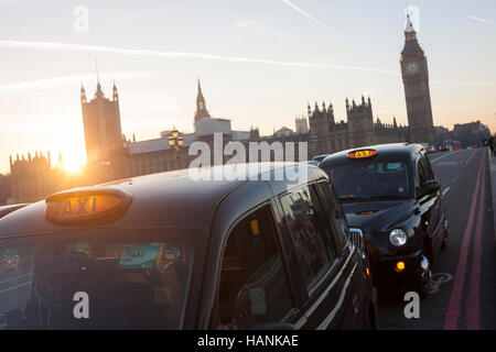 Mit einer untergehenden Sonne, Big Ben und den Houses of Parliament in der Ferne, werden zwei schwarzen Londoner Taxis auf Westminster Bridge wartet auf einen Tarif am 30. November 2016, in London, England gestoppt. Stockfoto