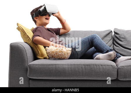 Kleiner Junge Verlegung auf einem Sofa mit VR-Brille und Essen Popcorn isoliert auf weißem Hintergrund Stockfoto