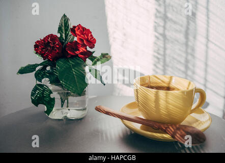 Gelbe Tasse Tee auf dem Tisch mit Blumen Stockfoto