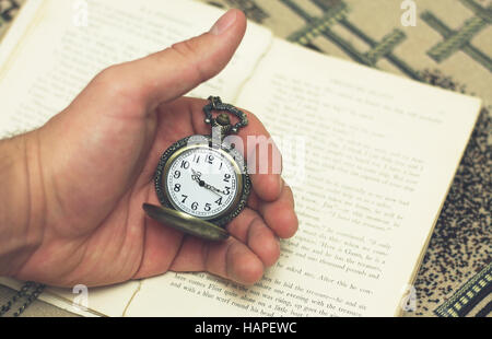 Alte Taschenuhr in der Hand auf dem Hintergrund des Buches Stockfoto