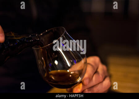 Man gießt schwarzen Bier aus der Flasche in Glas bei caffee Stockfoto