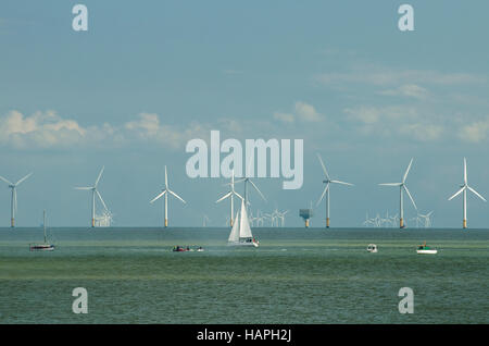 Eine Meereslandschaft zeigt kleine Boote/Yachten auf dem Wasser mit einem Hintergrund von Windenergieanlagen, am Meer. Stockfoto
