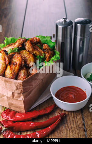 leckere gegrillte Hähnchenflügel mit Knoblauch und Tomaten-Sauce mit Salat in Essen Papiertüte auf hölzernen rustikalen Hintergrund Draufsicht, Witi Exemplar Stockfoto