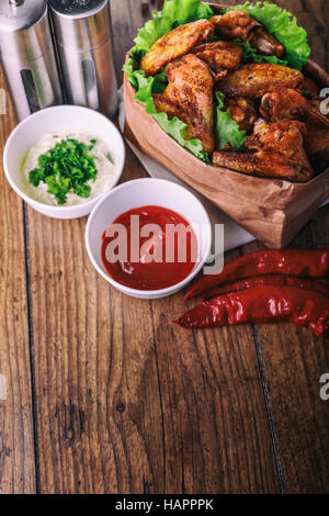 leckere gegrillte Hähnchenflügel mit Knoblauch und Tomaten-Sauce mit Salat in Essen Papiertüte auf hölzernen rustikalen Hintergrund Draufsicht, Witi Exemplar Stockfoto