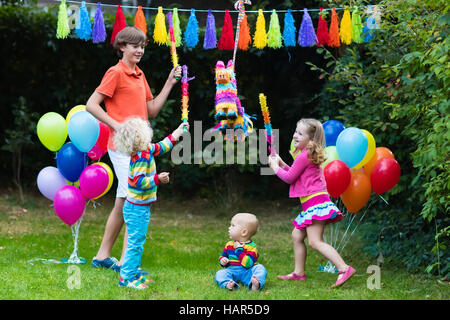 Kinder-Geburtstags-Party. Gruppe von Kindern schlagen Pinata, Spiel mit Luftballons. Familie und Freunde feiern Geburtstag im freien Stockfoto