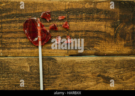 Rote Lollipo mit Herzform auf einem hölzernen Hintergrund gebrochen Stockfoto