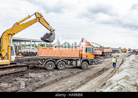 Gelbe Bagger füllt ein Muldenkipper mit Erde auf Baustelle, Projekt im Gange. Stockfoto