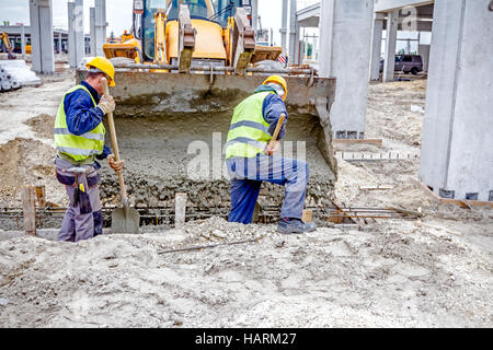 Arbeitnehmer sind mit gepanzerten konkretisiert, Loch im Boden mit Schaufeln ausfüllen. Stockfoto