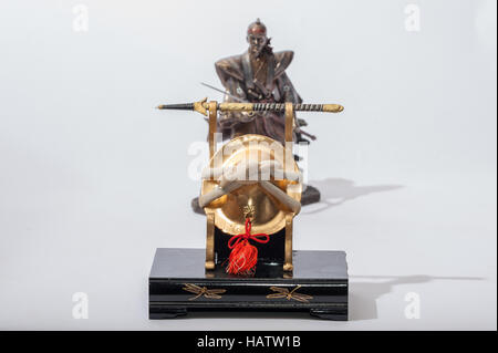 Miniatur-japanischen Kabuto-Helm und Schwert vor Statue von Samurai Stockfoto