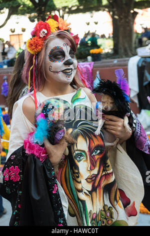 Eine Frau für tot Festivaltag in Tracht gekleidet zeigt ihren kostümierten Hunden am Jardin Principal in San Miguel de Allende, Guanajuato, Mexiko. Die einwöchigen Feier ist eine Zeit, als Mexikaner willkommen die Toten zurück für einen Besuch der Erde und das Leben feiern. Stockfoto