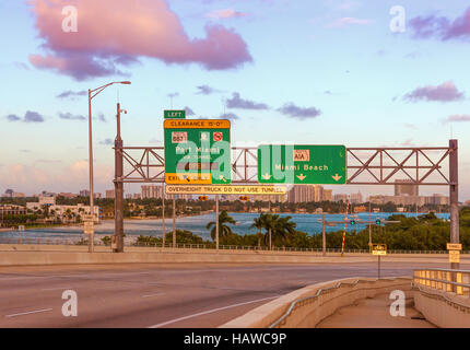Verkehrszeichen für Miami Beach, Florida, USA, am MacArthur Causeway bei Sonnenuntergang. Stockfoto