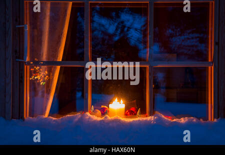 Verschneiten Abend Fenster eines Holzhauses. Auf der Fensterbank sind, Weihnachtsschmuck und brennenden Kerzen Stockfoto