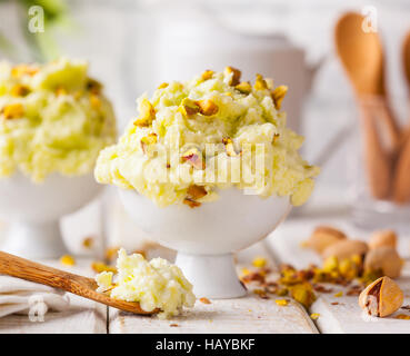 Eine Schüssel mit Pistazieneis mit gehackten Nüssen und Löffel auf einem rustikalen Hintergrund. Stockfoto