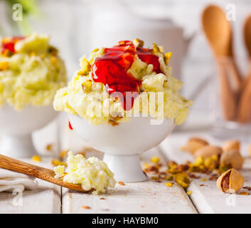 Eine Schüssel mit Pistazieneis mit gehackten Nüssen und Löffel auf einem rustikalen Hintergrund. Stockfoto