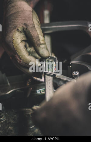 Hände halten einen digitalen Bremssattel und Messen des Abstands zwischen zwei Schrauben auf einem Motorrad Stockfoto