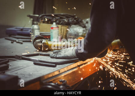 Arbeiter schneiden Stück Rundrohr mit einem Winkelschleifer auf einem Werkstatt-Tisch, Funken produzieren Stockfoto