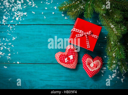 Weihnachtsbaum Zweig mit Schnee, rote Geschenkbox und zwei roten Herzen auf blauen Holztisch. Draufsicht mit Textfreiraum Stockfoto