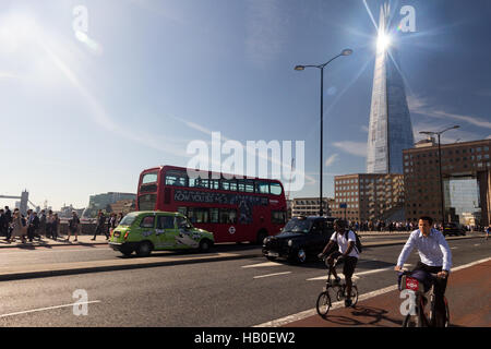 Radfahren über London Bridge während der morgendlichen Verkehr Arbeit, mit Sonnenlicht aus glänzenden Der Shard Gebäude im Hintergrund. Stockfoto