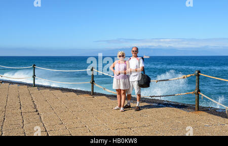 Älteres gegerbt paar in leichter Kleidung steht am Ufer Los Gigantes auf Teneriffa in der Sonne am strahlend blauen Wasser, Himmel Insel Gomera und tanken Stockfoto