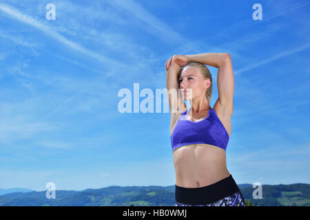 Junge Frau streckte ihre Arme bis während des Trainings auf einem Berg Stockfoto