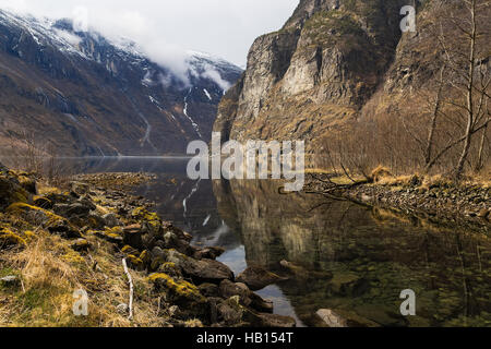 Der Fluss fließt von den felsigen Ufern im Fjord mit einem felsigen Berg im Hintergrund. Norwegen Stockfoto