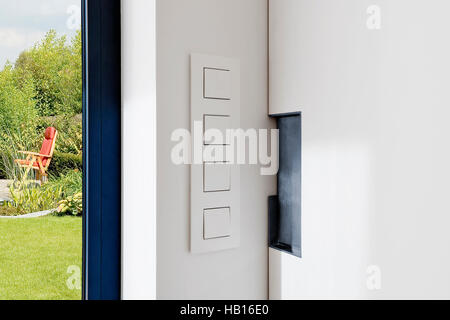 Lichtschalter in der Nähe einer Schiebetür in einer modernen Wohnung mit Blick auf einen üppigen Garten Stockfoto