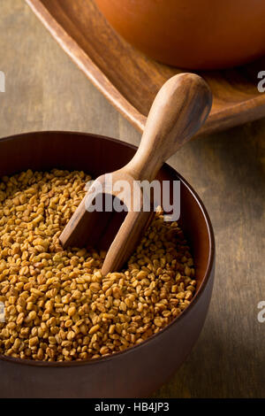 Gesamte unverarbeiteten Bockshornkleesamen (Trigonella Foenum-Graecumcumin) in Holzschale mit Schaufel Stockfoto