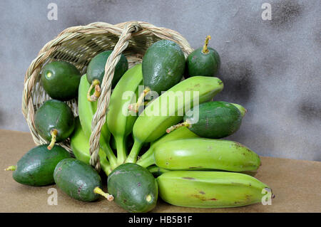 grüne Bananen und Avocados auf Korb Stockfoto