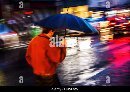 Bild mit Motion blur eines Mannes mit Regenschirm in der Nacht zu Fuß in die Stadt Stockfoto
