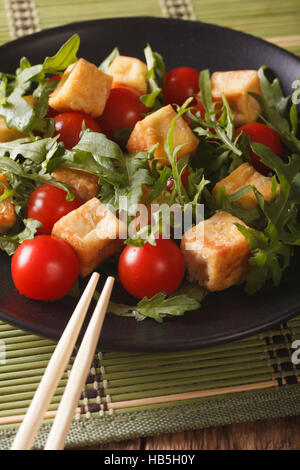 Asiatischer Salat mit gebratenem Tofu, Tomaten und Rucola Nahaufnahme auf einer Platte. Vertikal Stockfoto