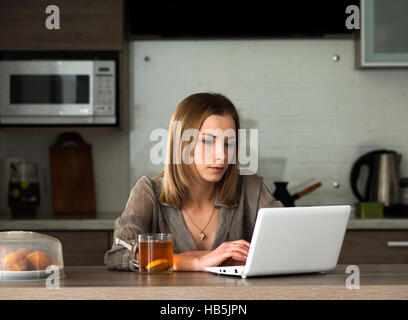 Junge schöne kaukasischen Frau Drinkig Tee und sieht Informationen im Bereich social Media auf Net-book Stockfoto