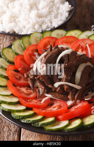 Kambodschanische Essen: Rindfleisch Lok Lak mit frischen Tomaten und Gurken Nahaufnahme auf einer Platte. vertikale Stockfoto