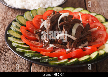 Kambodschanische Rindfleisch Lok Lak mit frischem Gemüse Nahaufnahme auf einer Platte. Horizontale Stockfoto