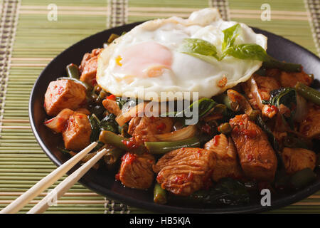 Thai Gai Pad Krapow Huhn mit Basilikum und Ei Nahaufnahme auf einer Platte. horizontale Stockfoto