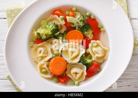 Italienische Tortellini-Suppe mit Broccoli, Erbsen, Karotten und Paprika Nahaufnahme auf dem Teller auf den Tisch. Horizontale Ansicht von oben Stockfoto