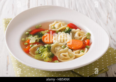 Italienische Tortellini-Suppe mit Broccoli, Erbsen, Karotten und Paprika Nahaufnahme auf dem Teller auf den Tisch. horizontale Stockfoto