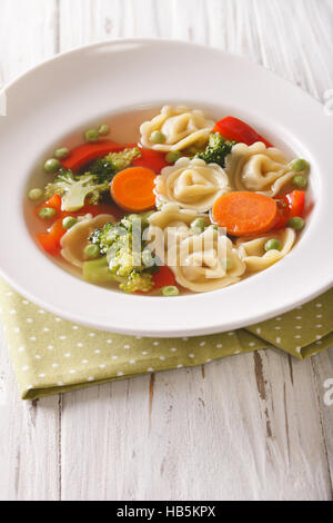 Heißen Tortellini-Suppe mit Broccoli, Erbsen, Karotten und Paprika Nahaufnahme auf dem Teller auf den Tisch. vertikale Stockfoto